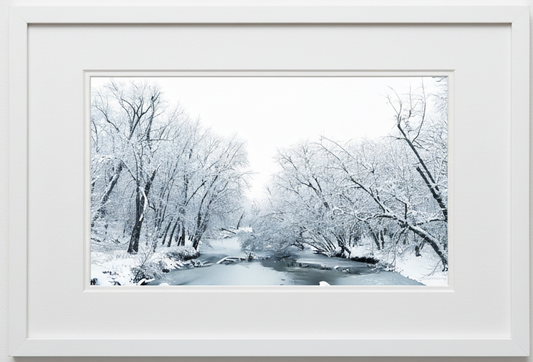 Framed winter landscape with snow-covered trees and a stream.