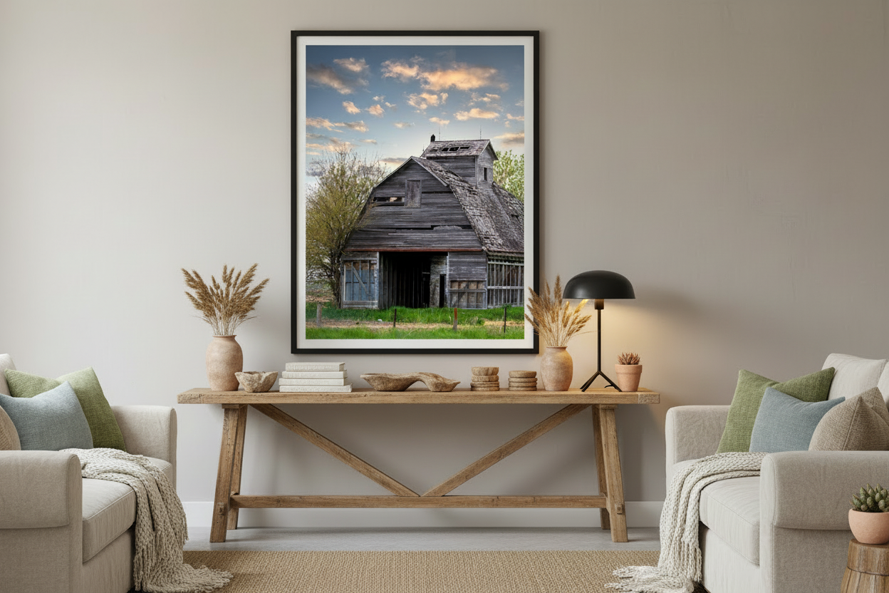 Framed photograph of a rustic iowa barn on a wall in a living room with a wooden table and beige sofa.