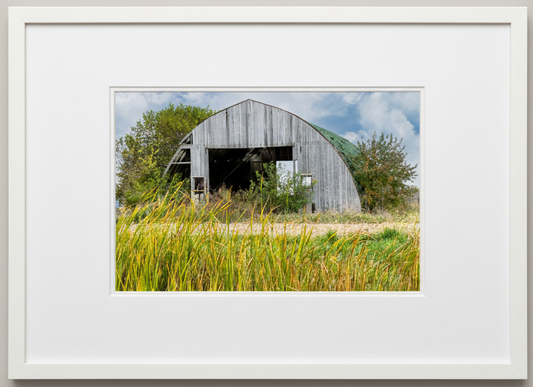 Framed photograph of a rustic wooden barn in a field with tall grass.