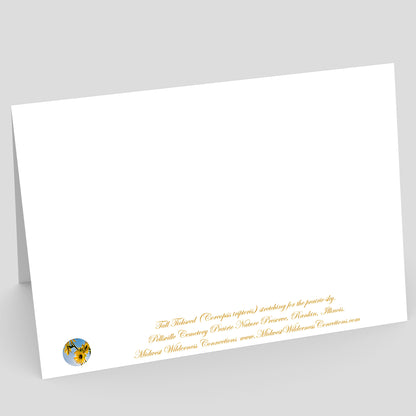 View of the backside of a white greeting card card with gold text and a logo on a gray background. The text, which is along the bottom edge, describes the photo on the front of the card and where the photo was  taken