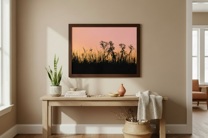 Framed artwork of a sunset over grass on a wall in a room with a wooden bench and decor items.