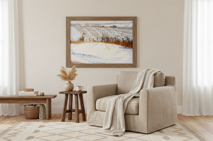 Living room with beige armchair, wooden coffee table, and framed photo print of a winter landscape of farm fields on the wall.