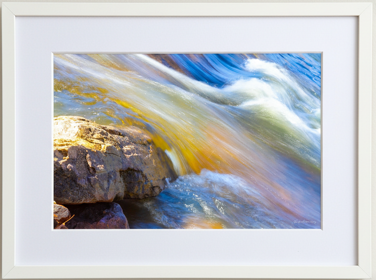 Framed photograph of a colorful stream flowing over rocks