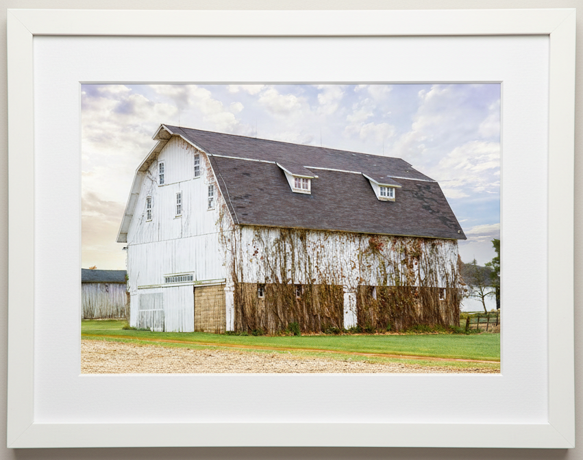 Framed photograph of a midwest white barn with a gray roof against a blue sky in illinois 