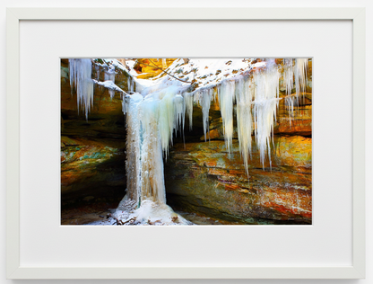 A white Framed photograph of arock bluffs with a waterfall frozen in ice at wild cat den state park in iowa