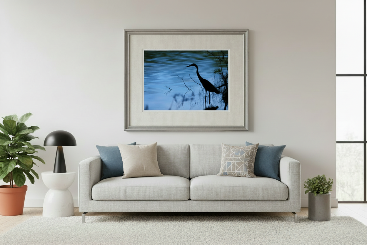 Framed artwork of a heron silhouette over water on a wall above a sofa in a living room.