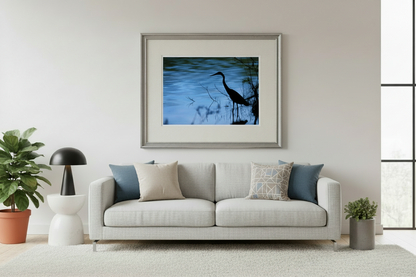 Framed artwork of a heron silhouette over water on a wall above a sofa in a living room.