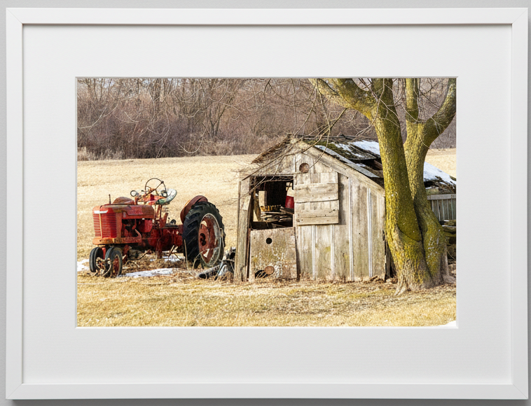 Antique Red tractor and wooden shed in a rural Iowa setting with a white frame.