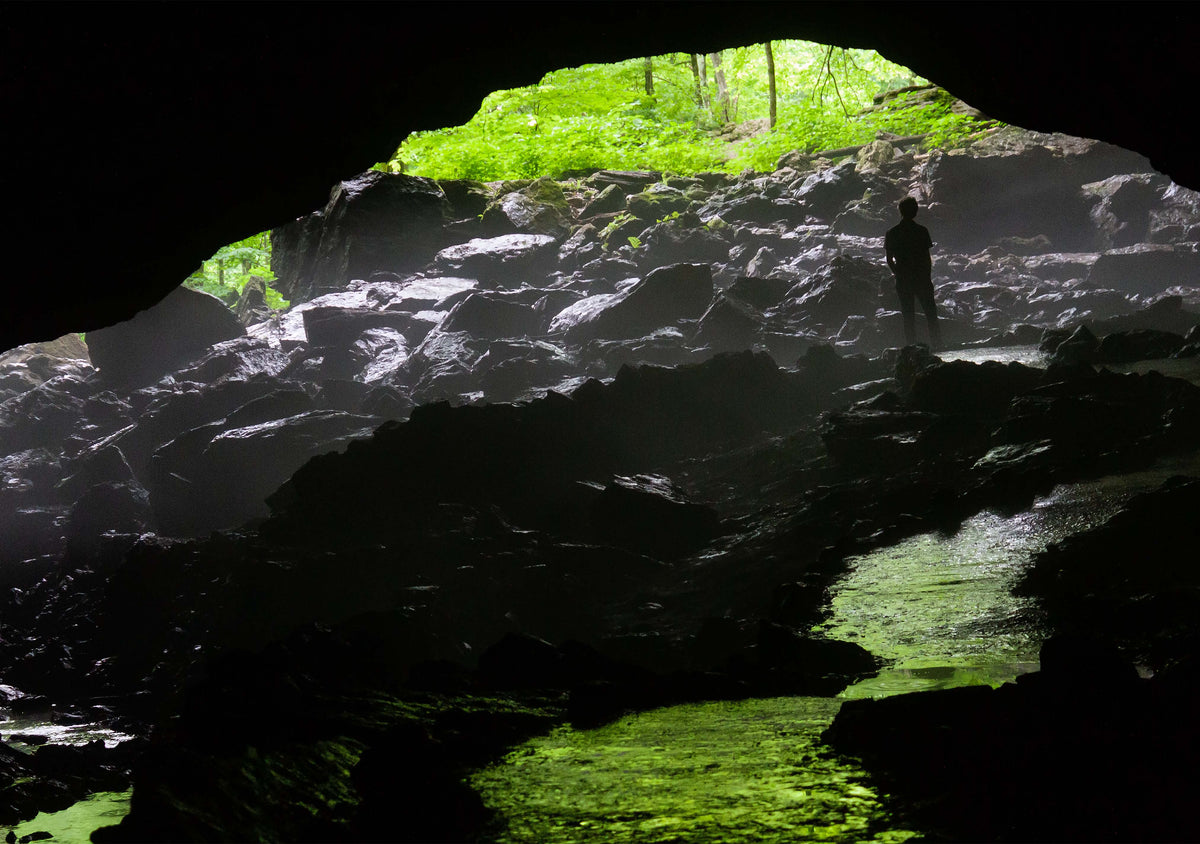 A photo print featuring a person standing in a cave with a blurred greenery background, indicative of the natural setting of the cave at maquoketa caves state park in iowa